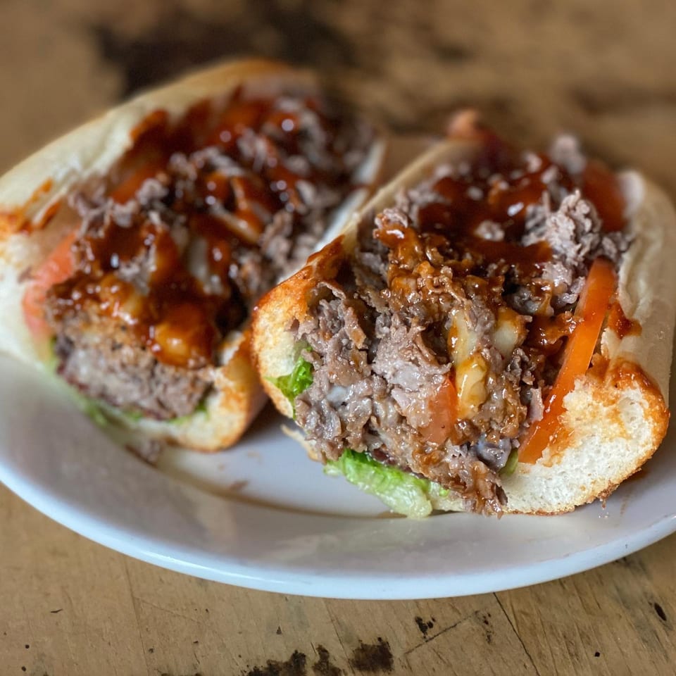 Two saucy chopped-beef sandwiches with lettuce and tomatoes on a white plate atop a wooden table.