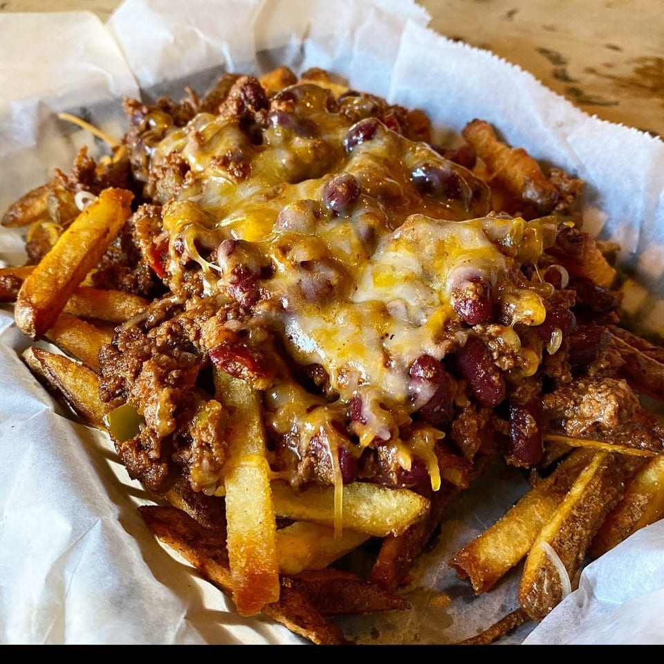 Crispy fries piled with seasoned ground beef, kidney beans, peppers, and melted cheese in a paper-lined basket.