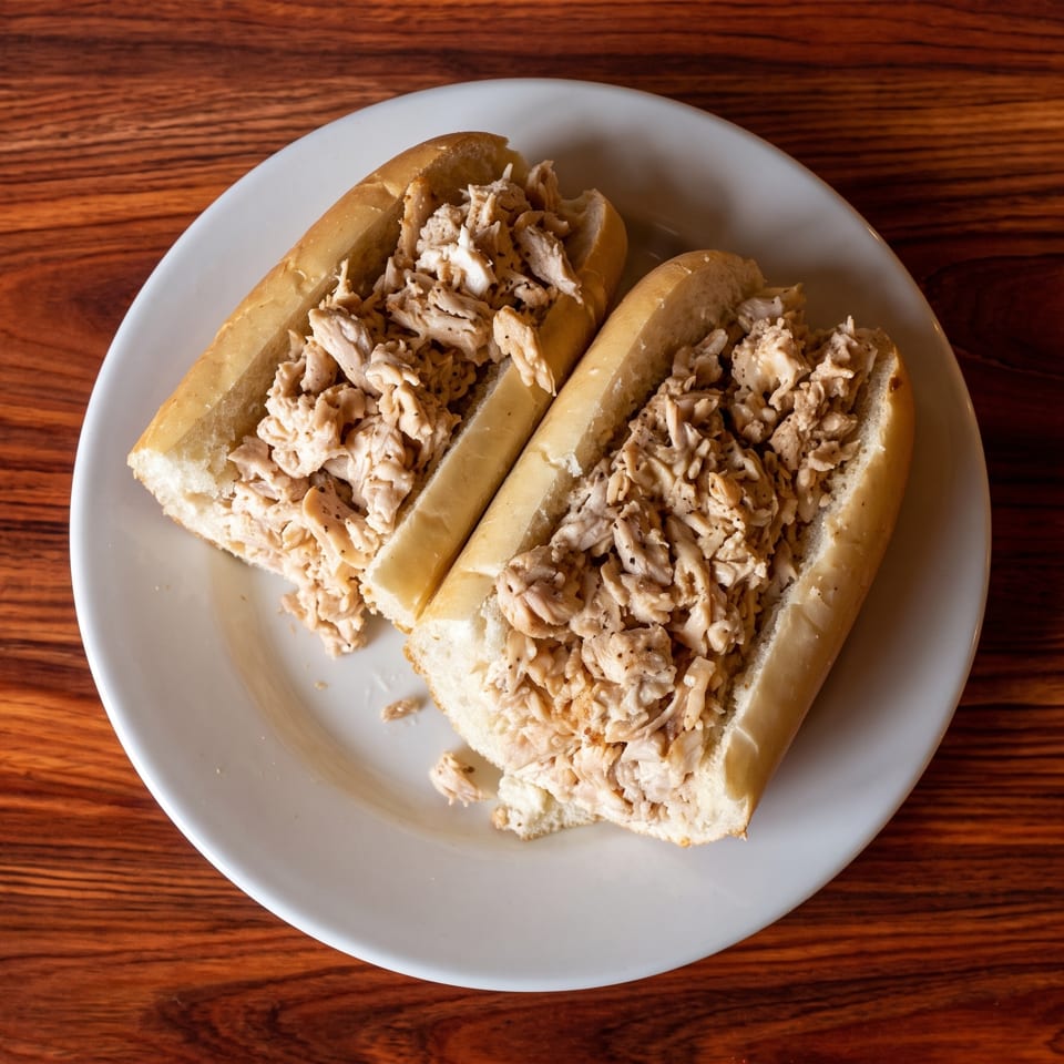 Two chicken salad subs on a white plate, resting on a dark wooden table.