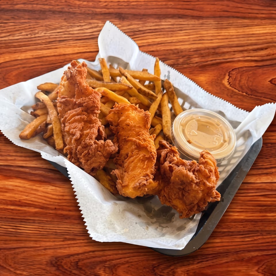 Crispy fried chicken tenders and golden french fries in a basket with dipping sauce on a wooden table.